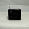 A black, rectangular ADP250A405J 4 uF 250 VAC Capacitor (model 6100-9133) with two metal prongs on top is placed on a light textured surface.