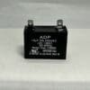 A black rectangular ADP250E156J 15 μF 250 VAC capacitor with two metal prongs on top is placed on a white surface. The label displays its capacitance (15 μF), voltage rating (250 VAC), frequency range (50/60 Hz), and several certification markings.