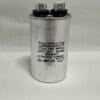 A Scotsman 18-1902-65 Run Capacitor (model CBB65-440R1755, 17.5 μF, 440 VAC) with a silver cylindrical body, top-mounted electrical terminals, and black printed specifications including its capacitance and voltage ratings (-40°C to +70°C) is standing upright on a white surface.