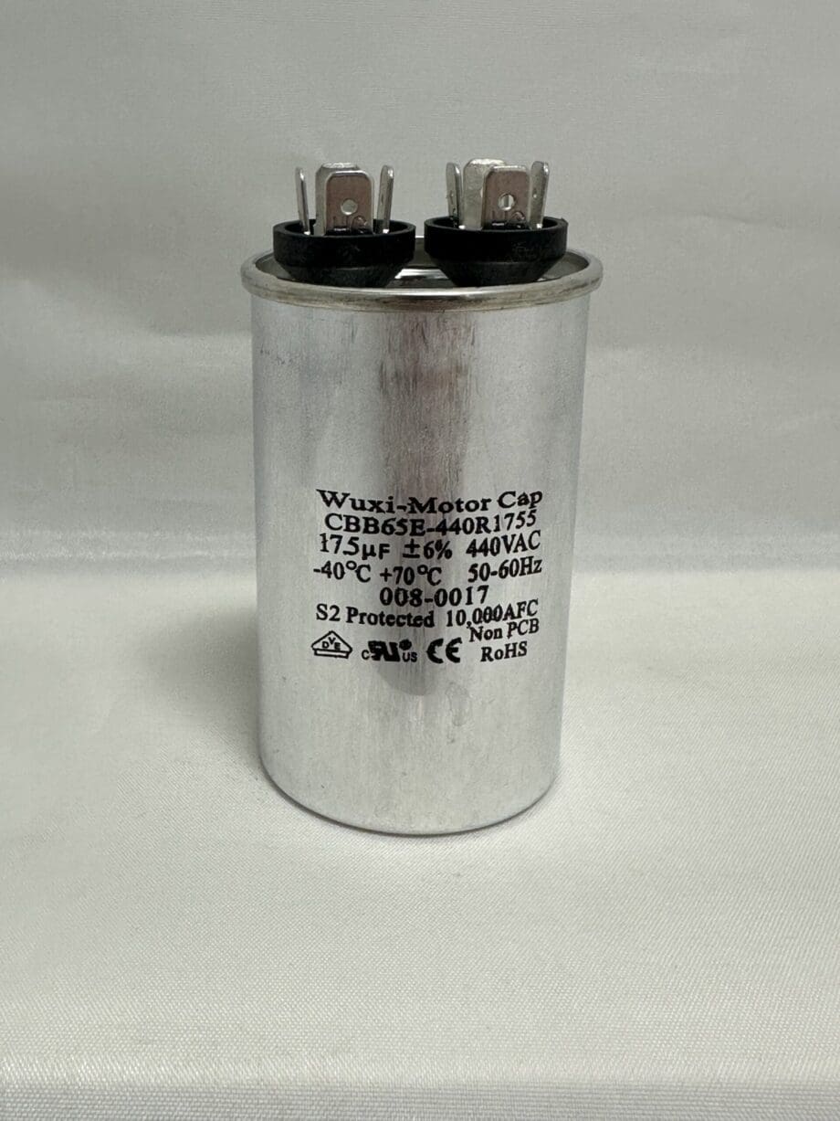 A Scotsman 18-1902-65 Run Capacitor (model CBB65-440R1755, 17.5 μF, 440 VAC) with a silver cylindrical body, top-mounted electrical terminals, and black printed specifications including its capacitance and voltage ratings (-40°C to +70°C) is standing upright on a white surface.