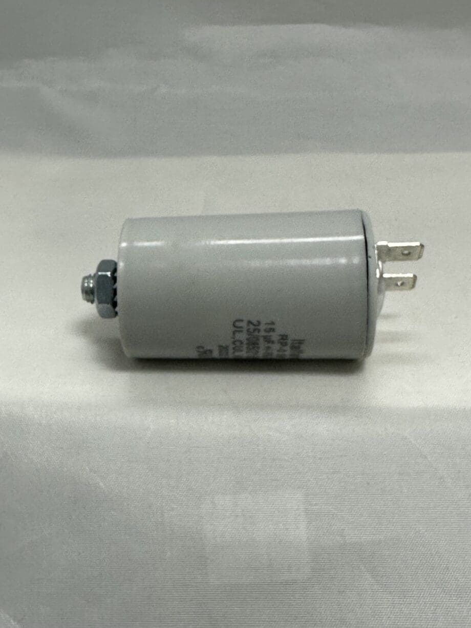 A RPN0E156M8-M1 15 uF 250 VAC gray cylindrical capacitor with metal terminals and a bolt on one end, lying on a white surface.
